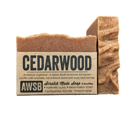 A Wild Soap Bars Cedarwood soap, enriched with Moroccan red clay, has textured edges and is partially wrapped in rustic brown paper. The label reads Cedarwood, highlighting juniperus virginiana, a fresh forest scent, and an exfoliating texture.