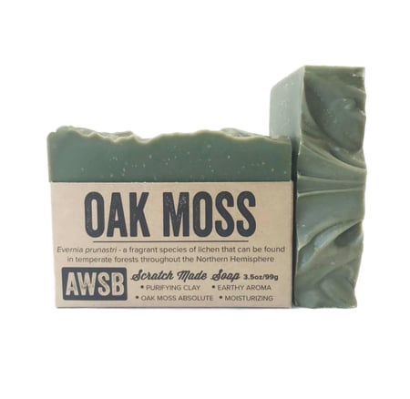 A Wild Soap Bars Oak Moss is a green textured soap exuding a robust mens scent. The packaging states Scratch Made Soap and highlights its purifying clay, earthy oakmoss aroma, and moisturizing qualities. Weight: 3.5oz/99g.