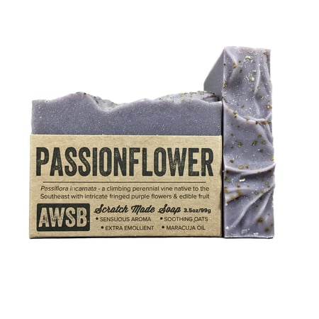 The A Wild Soap Bar - Passionflower from A Wild Soap Bar is a purple, textured soap bar partly wrapped in brown paper. The packaging highlights soothing oats, maracuja oil, and ylang ylang essential oil for extra emollient properties.