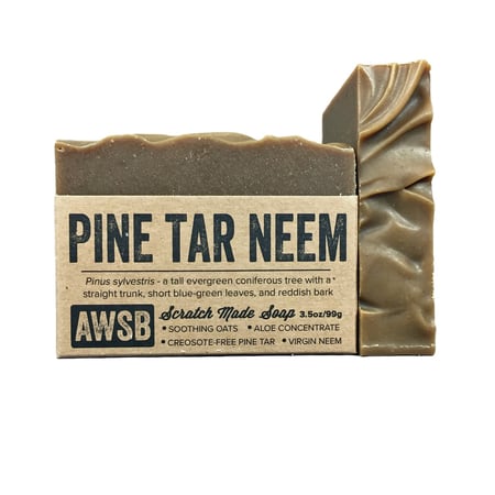 A Wild Soap Bars Pine Tar Neem, partially nestled in brown packaging, features soothing oats, organic neem oil, aloe concentrate, creosote-free pine tar, and tea tree essence.