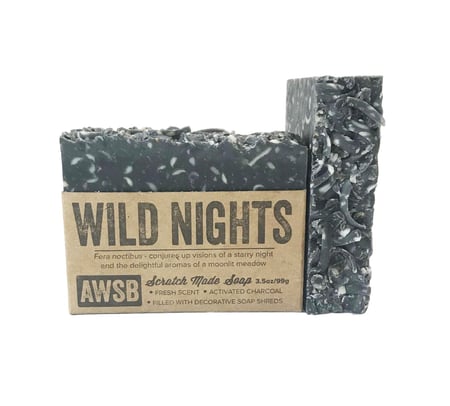 A black speckled bar of A Wild Soap Bar - Wild Nights wrapped in brown, exemplifying zero waste. Infused with activated charcoal and sherbet matte finish, it has decorative soap shreds and essential oils for rejuvenating cleansing.