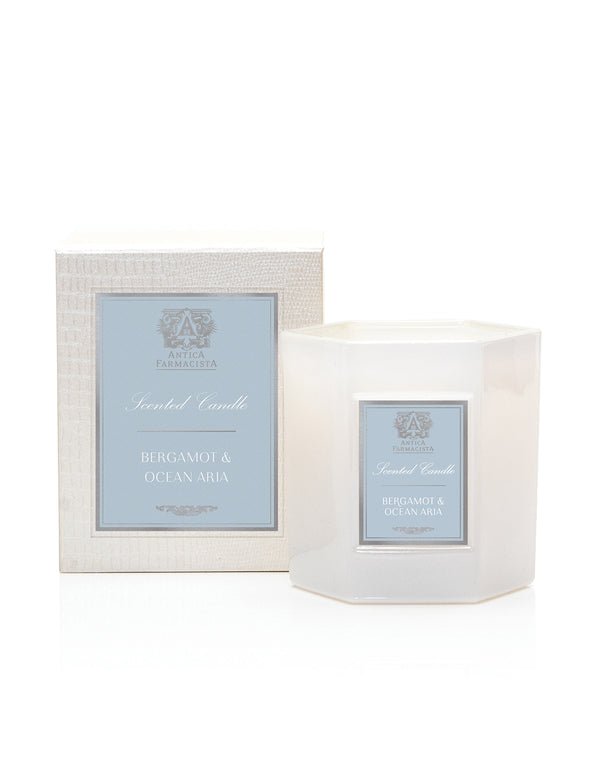 The Antica Farmacista - Bergamot & Ocean Aria candle is elegantly placed in a hexagonal white glass container with a beige box. Both feature a blue label and are made from soy-paraffin wax, exuding minimalist charm and oceanic notes.