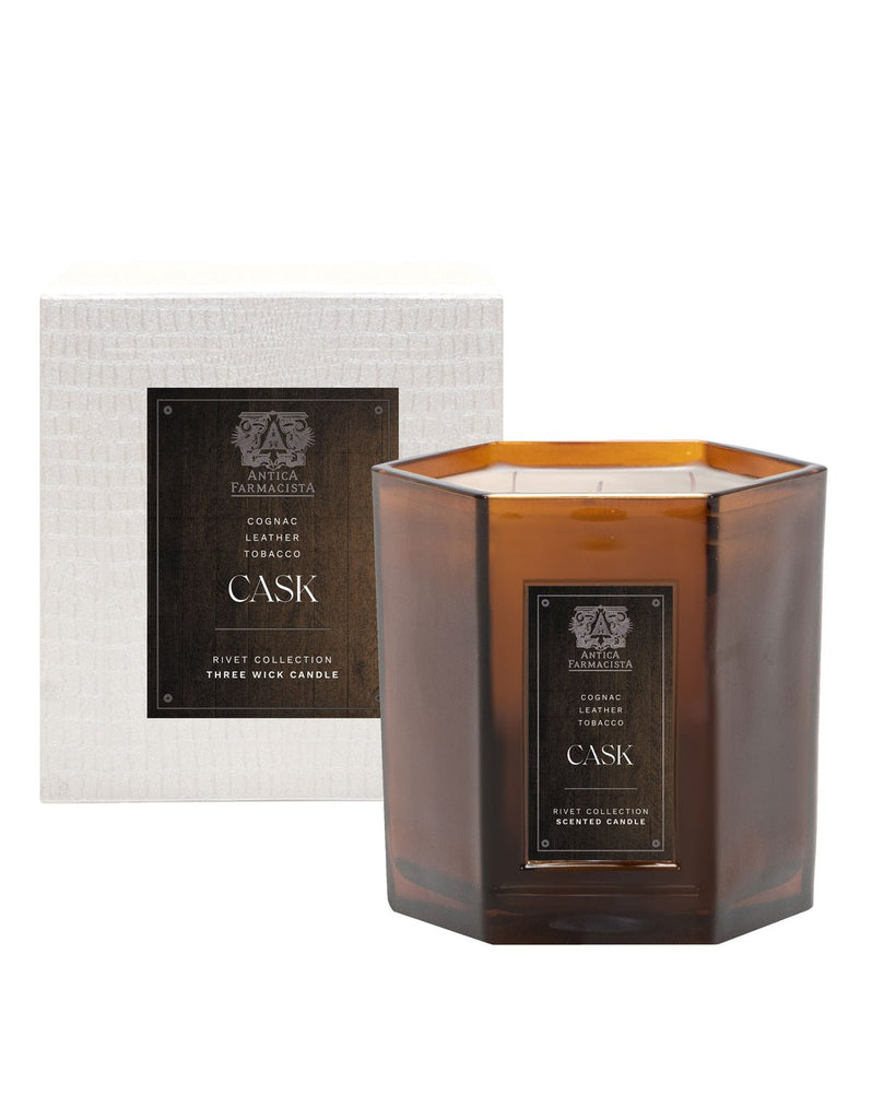 A hexagonal brown candle with a black Cask Candle label stands in front of a matching textured box. The luxury fragrance, part of Antica Farmacistas Rivet Collection, offers an elegant experience with its three wicks.