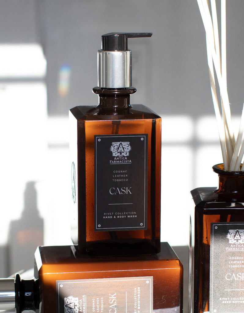 The Antica Farmacista Cask hand & body wash, 16oz, from the Rivet Collection features a rich Cognac & Tobacco scent and natural ingredients. It comes in a brown bottle with a pump dispenser, set against a blurred background with another similar bottle partly visible beside it.