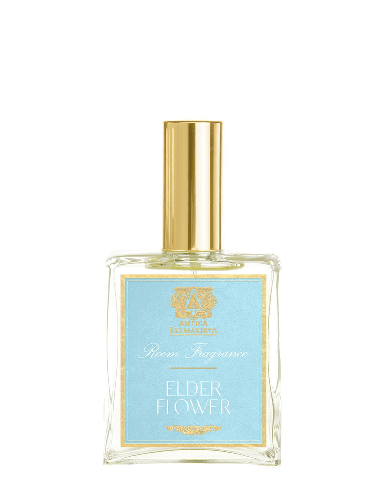 The Antica Farmacista - Elder Flower 100ml Room Spray, with a light blue label and gold accents, captures botanical poetry. Its clear glass bottle, elegant design, and golden cap add a refined touch to any space.