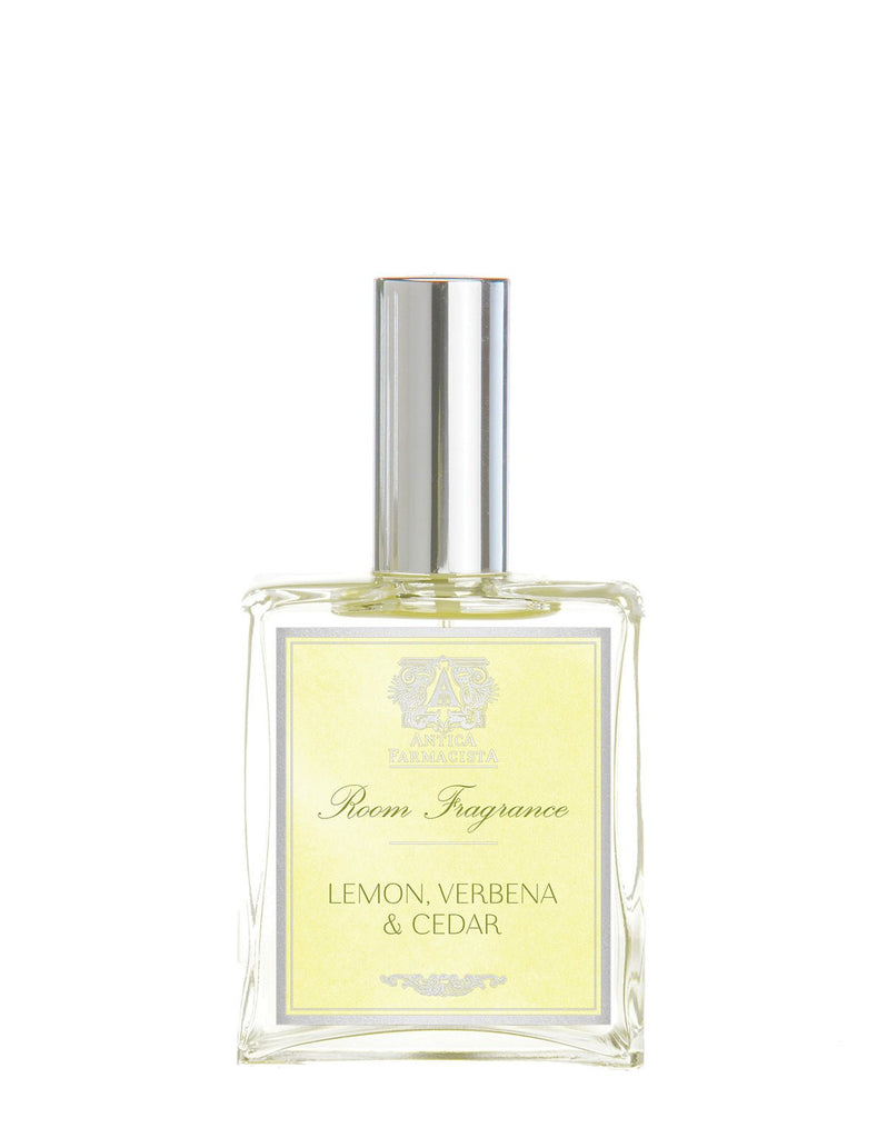 A clear glass bottle with a silver cap labeled Antica Farmacista - Lemon, Verbena & Cedar 100ml Room Spray contains a yellowish liquid promising a refreshing fragrance, featuring decorative detailing.