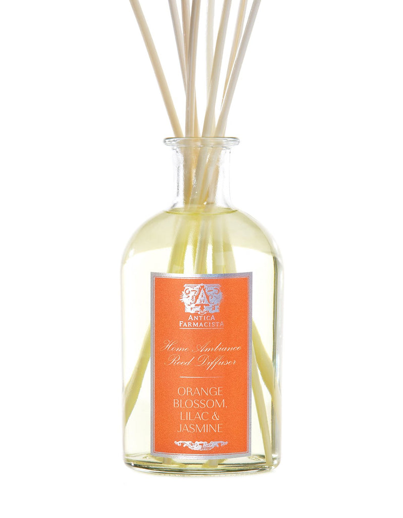 A 250ml Antica Farmacista reed diffuser features light orange liquid and reeds. The label, Orange Blossom, Lilac & Jasmine, highlights the scent of delicate jasmine with vibrant orange blossom.