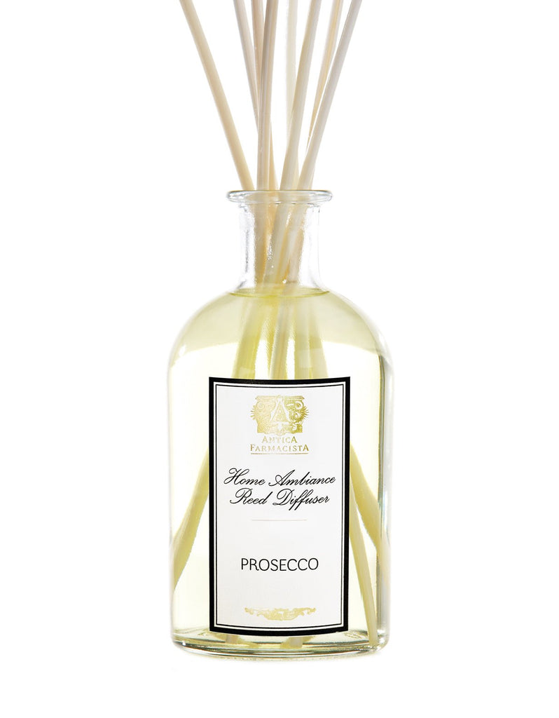 The Antica Farmacista - Prosecco 250ml Reed Diffuser features a clear glass bottle with light yellow liquid and white reeds. Its elegant label has ornate details, adding style to any home ambiance.