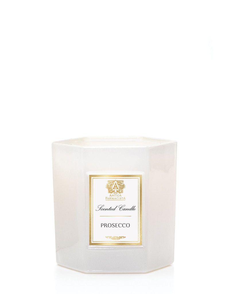 The Antica Farmacista - Prosecco 9oz Candle features a white hexagonal glass with a gold-trimmed label, reading Prosecco Candle. The glass is translucent with intricate top detailing that complements the hints of Madagascar Vanilla against a plain white background.