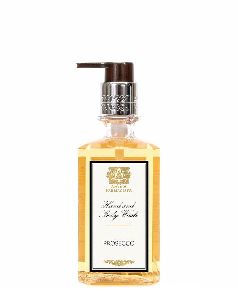 The 10oz Antica Farmacista Prosecco Hand & Body Wash comes in a clear bottle with a brown pump, showcasing a gold and white label. The light amber liquid is elegantly marked with Prosecco and hints of Madagascar Vanilla near the bottom.