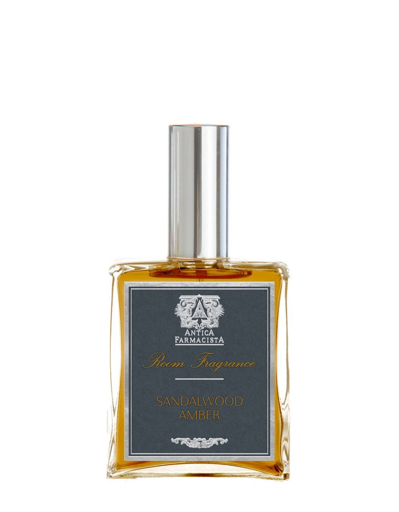 The Antica Farmacista - Sandalwood Amber 100ml Room Spray features a sleek rectangular bottle with a metallic cap and amber liquid, boasting a stylish label that captures luxury in every spritz.