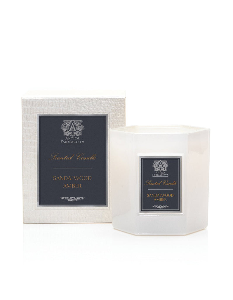 An Antica Farmacista - Sandalwood Amber 9oz Candle, a white hexagonal soy-paraffin blend in a clear holder, is labeled and elegantly boxed from the Rivet Collection on a pristine white background.