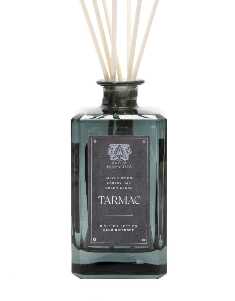 A 320ml dark green glass reed diffuser by Antica Farmacista, labeled Tarmac, emits sandalwood, silver wood, earthy oak, and green cedar scents. Natural reeds extend from the bottles opening.