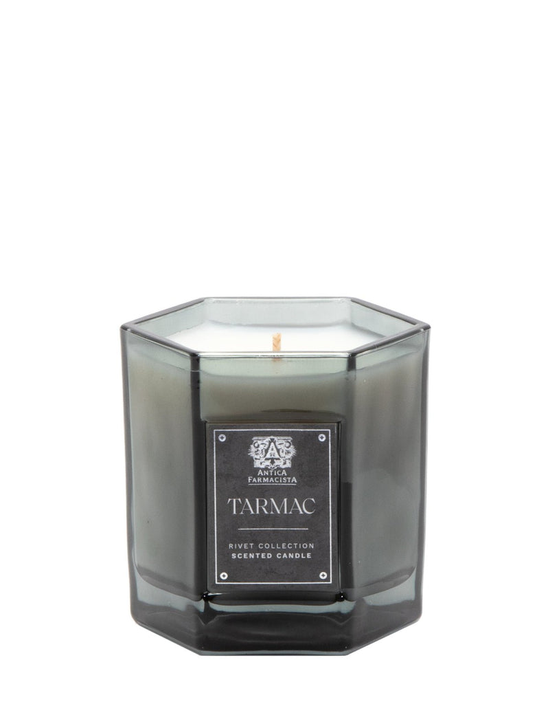 The Antica Farmacista Tarmac 9oz Candle from the Rivet Collection is a gray-tinted hexagonal glass candle with a soy-paraffin blend and a single wick wrapped in white wax. The brand logo is elegantly positioned above the label, enhancing its sophisticated appeal.