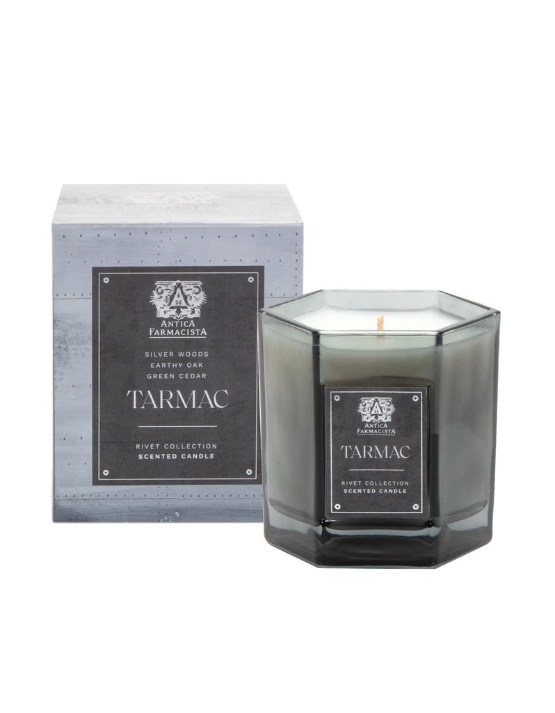 The Antica Farmacista - Tarmac 9oz Candle from the Rivet Collection is elegantly packaged in grey. This hexagonal beauty releases silver woods, earthy oak, and green cedar aromas from its soy-paraffin wax blend.