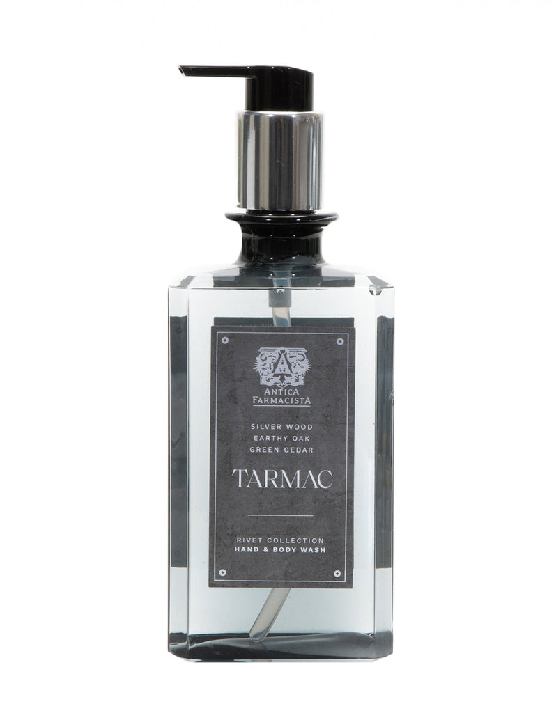 The Antica Farmacista Tarmac Hand & Body Wash comes in a rectangular bottle with a pump dispenser. Part of the Rivet Collection, it features an earthy scent blend of Silver Wood, Oak, Cedar, and Black Pepper. The transparent bottle is adorned with a dark label and silver cap.