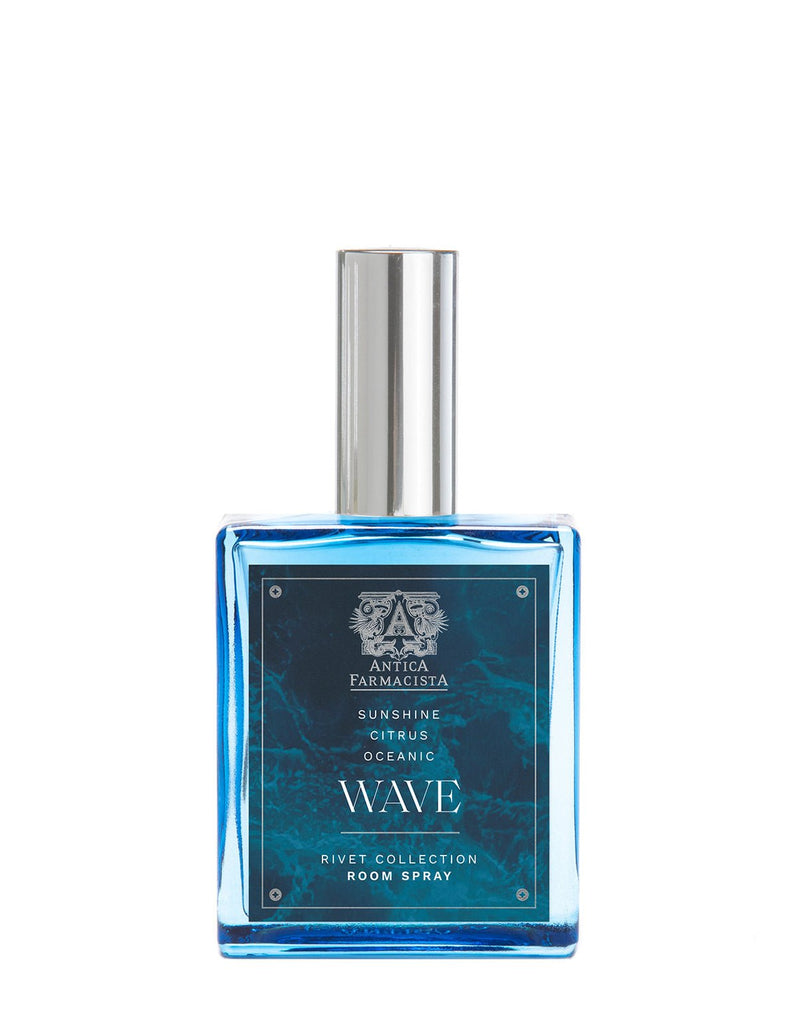 A blue glass bottle of Antica Farmacista - Wave 100ml Room Spray from the Rivet Collection features a rectangular design with a silver cap and a decorative wave-patterned label. The elegant home fragrance is labeled Sunshine Citrus, Oceanic Wave.