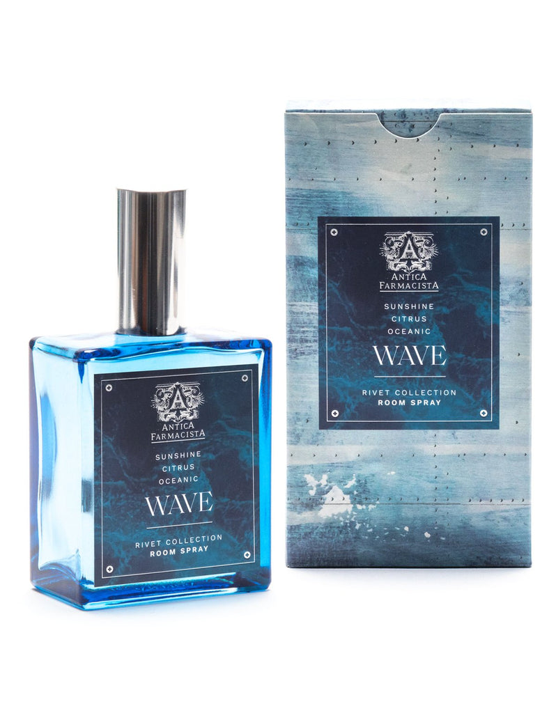 An Antica Farmacista Wave 100ml Room Spray with a silver cap sits next to its matching blue box. The label highlights Antica Farmacista, evoking sunshine, citrus, and ocean scents. The wave-inspired design suggests a fresh coastal breeze.