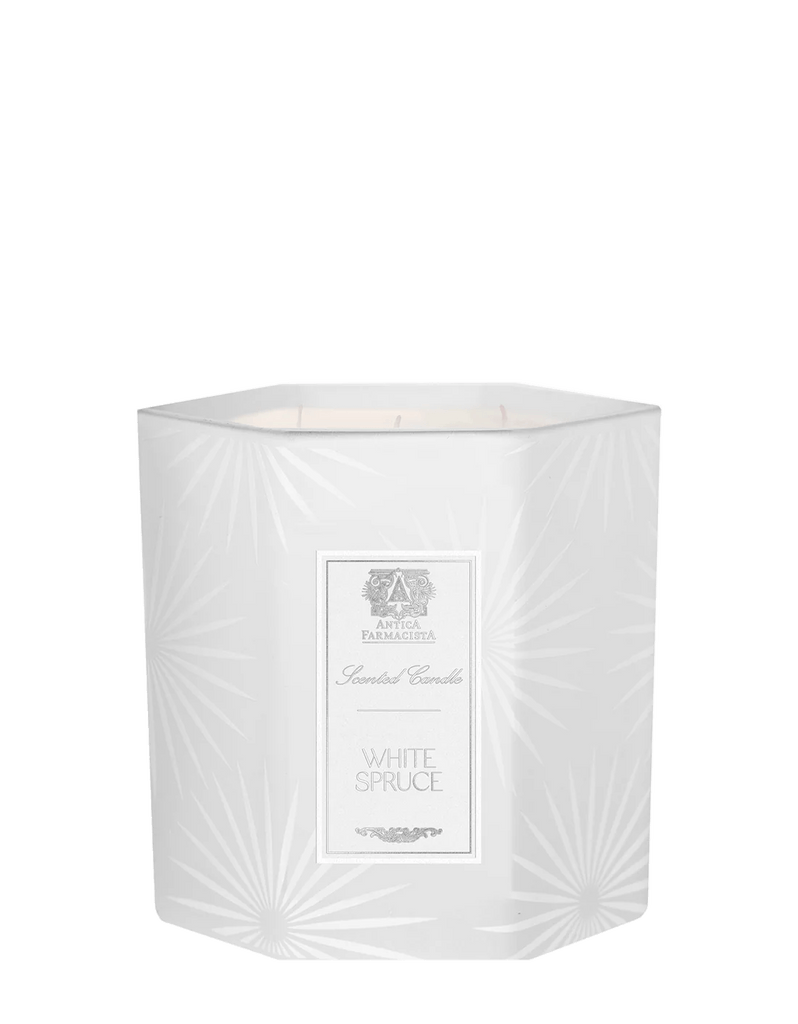 The Antica Farmacista White Spruce Three-Wick Candle features a decorative hexagonal container with a subtle starburst pattern and an elegant label, capturing fresh cut spruce in its sophisticated design.