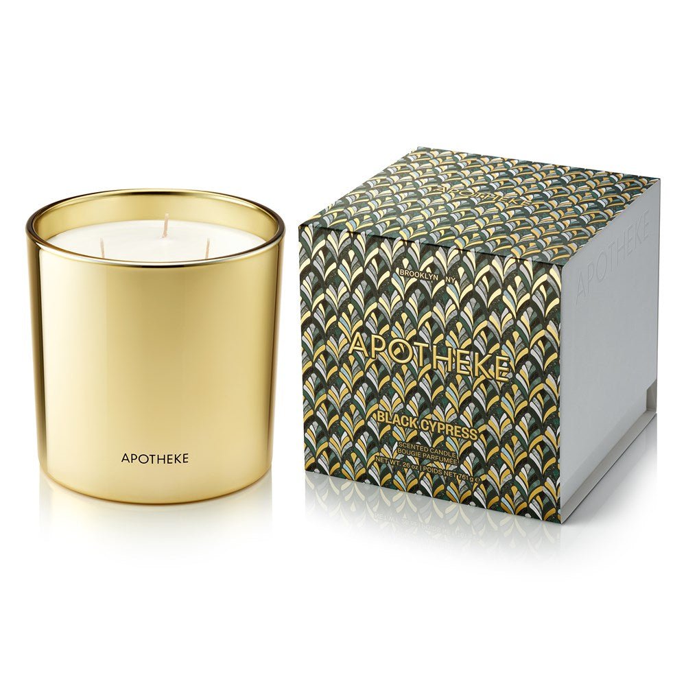 The Apotheke Black Cypress 3 Wick 72oz candle, made from a soy wax blend, sits elegantly beside its decorative box adorned with gold, blue, and green leaves. Both the candle and box feature the Black Cypress label, while APOTHEKE is stylishly inscribed on the container.