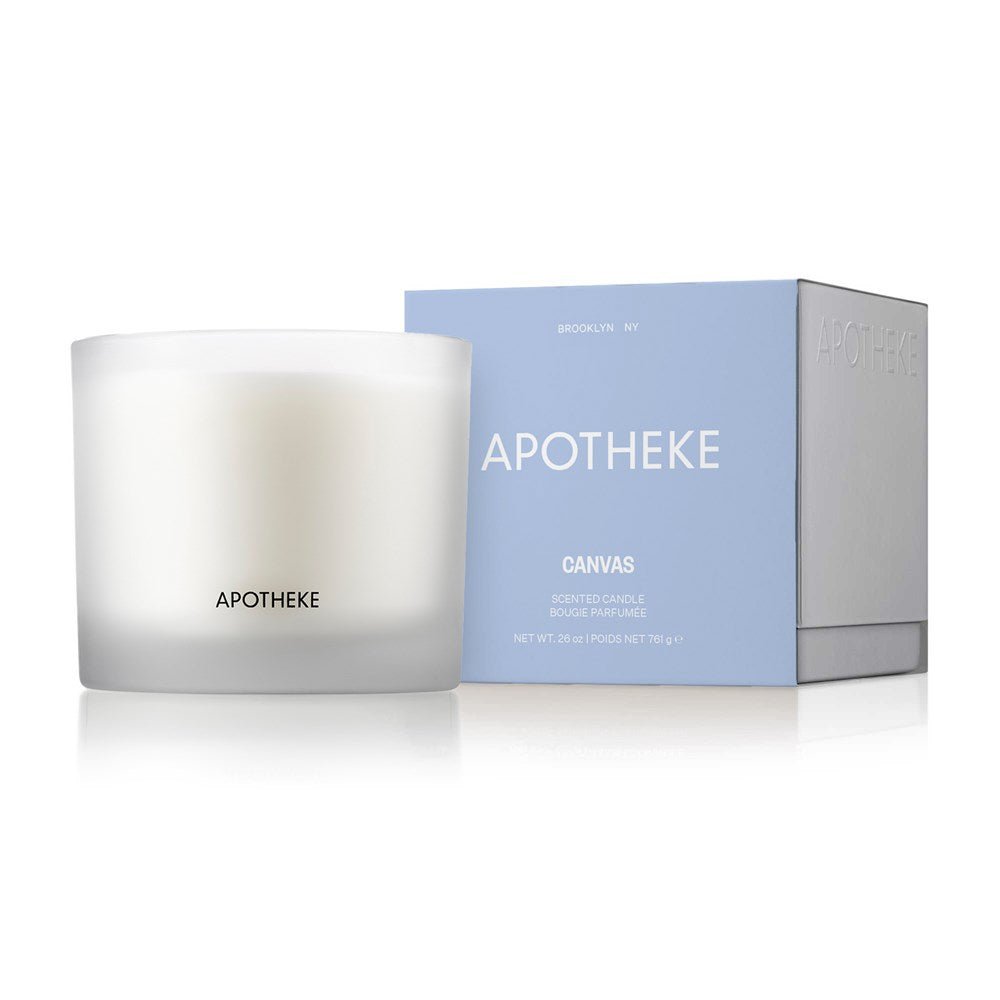 A white Apotheke Canvas 3-Wick Candle in a frosted glass holder sits beside a branded blue and white box. The box showcases product details, including the soy wax blend and essential fragrance oils, all elegantly set against a pristine white background.