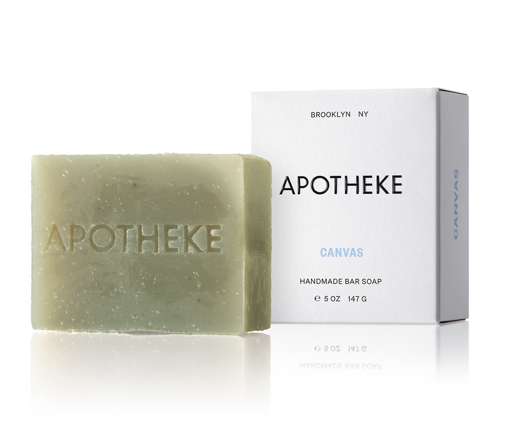 A green Apotheke - Canvas Bar Soap, embossed with APOTHEKE, is in front of the white box labeled BROOKLYN NY, APOTHEKE, and HANDMADE BAR SOAP, 5 OZ (147 G). The plant-based soaps elegant packaging stands upright.