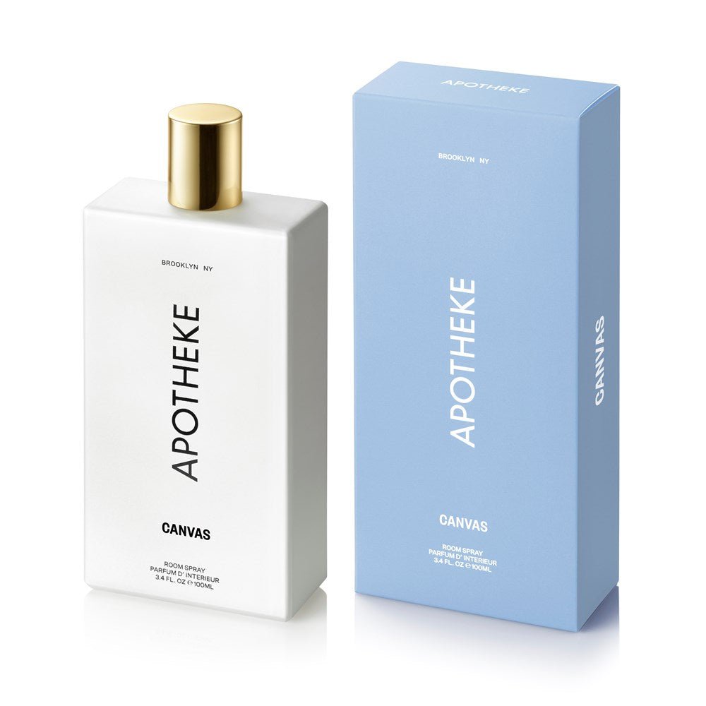 A gold-capped perfume bottle labeled Apotheke - Canvas Room Spray stands next to a branded blue box. Featuring essential oils, it offers a refreshing scent. The text BROOKLYN, NY appears above the brand name on the bottle.