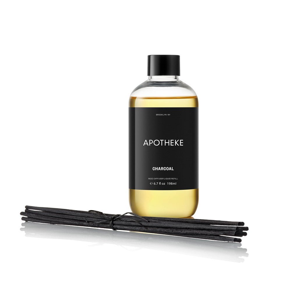 An Apotheke Charcoal Reed Diffuser Refill is showcased upright with a black label and yellowish oils. Several black reeds lie horizontally beside it, ready to rejuvenate your space.