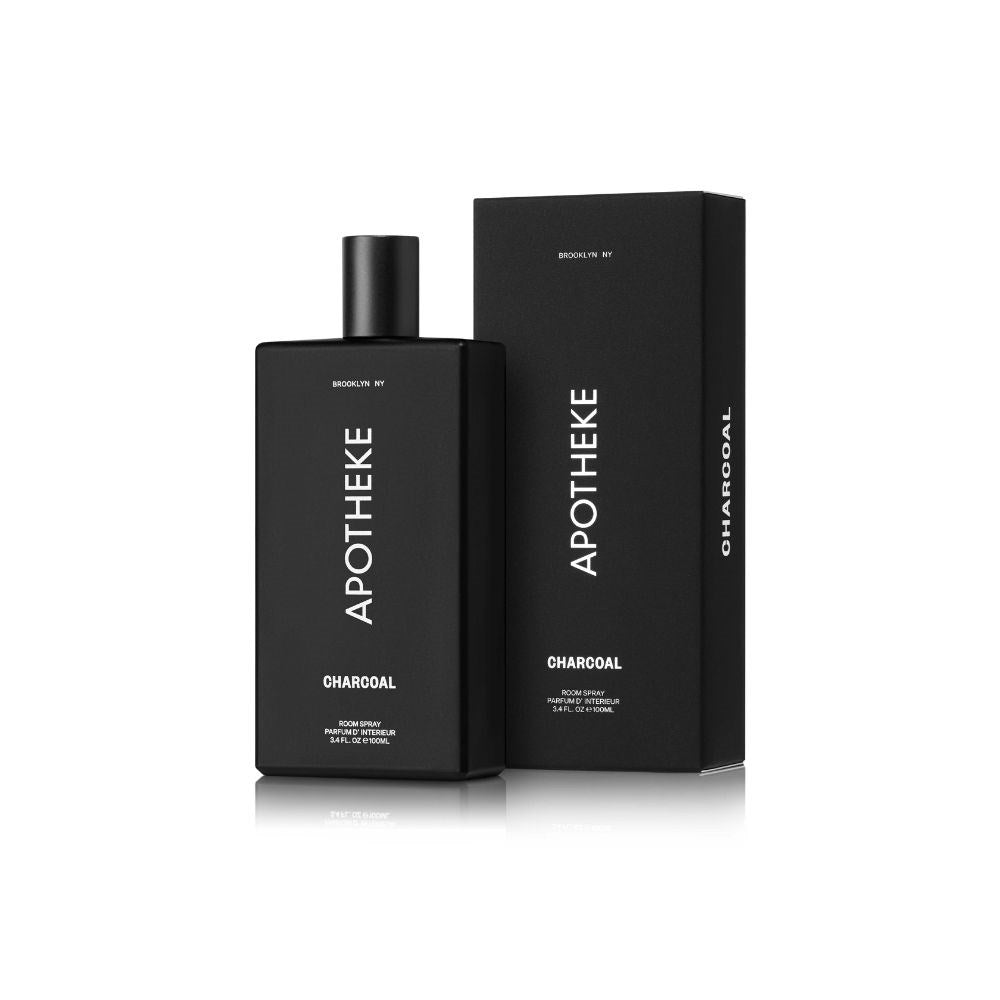 A black rectangular bottle and matching box of Apotheke Charcoal Room Spray are set against a white backdrop. Featuring minimalist design with white text, this woody fragrance evokes luxury. Both items display the brand name, Apotheke, and product details.