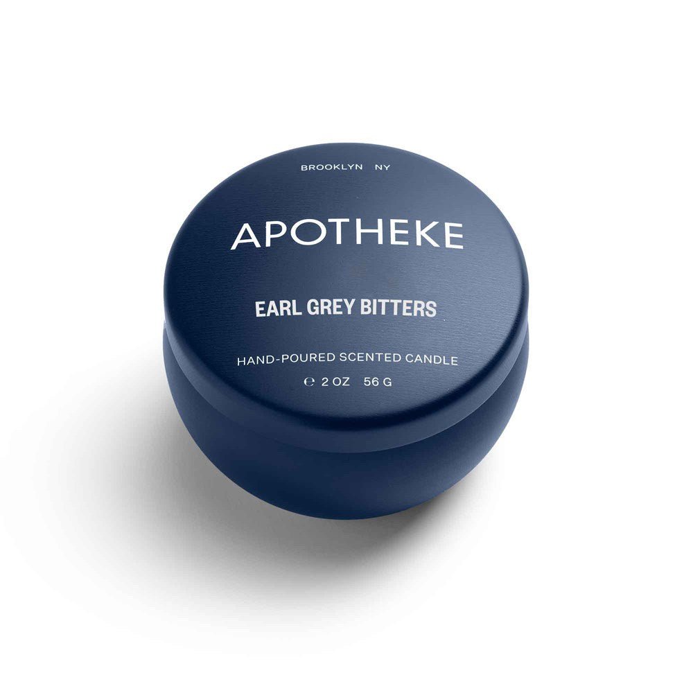 A 2 oz, 56 g navy blue candle tin from Apotheke displays Earl Grey Bitters with citrusy bergamot underneath. It reads Brooklyn NY at the top and is labeled as a hand-poured soy wax blend scented candle.