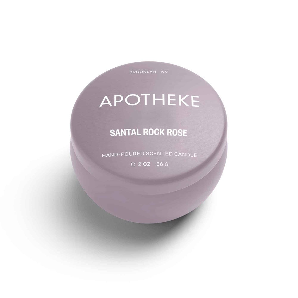 A 2 oz hand-poured luxury scented candle labeled Apotheke - Santal Rock Rose, crafted from a soy wax blend, rests in a lavender round tin. Brooklyn NY is above the brand name. The closed tin casts a soft shadow on a white background.