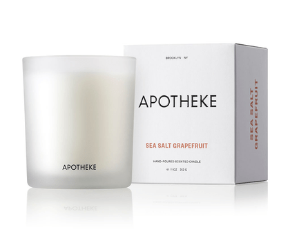 A frosted white glass candle labeled Apotheke - Sea Salt Grapefruit 10.5oz Candle sits next to a matching box, which reads HAND-POURED SOY WAX CANDLE. The citrus scent of this Apotheke product shines through its clean, minimalist packaging.