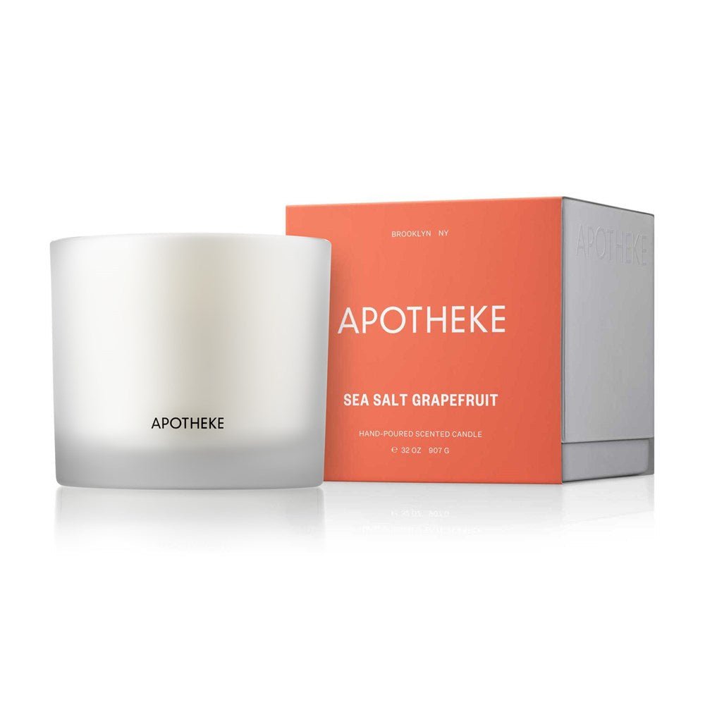 A white Apotheke - Sea Salt Grapefruit 3-Wick Candle in a frosted jar is shown beside its orange box, which beautifully highlights the candles name and citrus fragrance details.