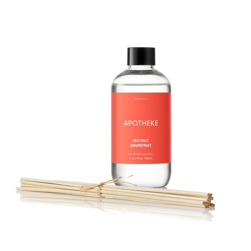 A clear bottle with a red label Apotheke - Sea Salt Grapefruit Reed Diffuser Refill showcases a citrus-scented refill, accompanied by wooden reeds.