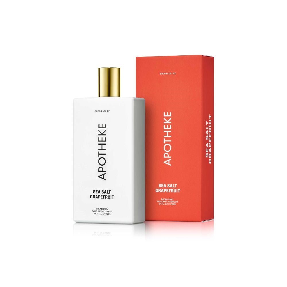 The Apotheke Sea Salt Grapefruit Room Spray features a white bottle with a gold cap, exuding a refreshing citrus fragrance. Its showcased beside its vibrant red box, both boldly displaying the product name in crisp white letters against the plain white background.