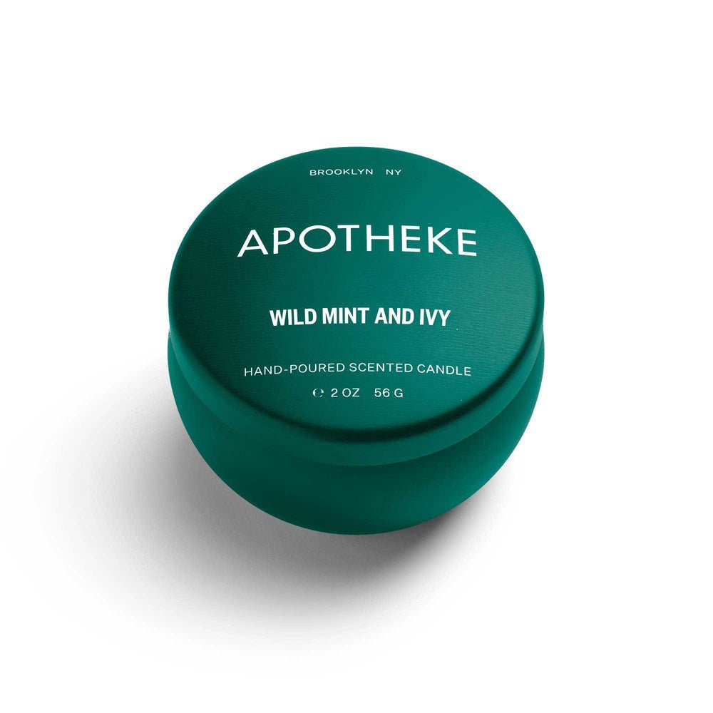 A small, round, dark green tin candle with a lid on a white background. The label reads Apotheke - Wild Mint And Ivy Mini Tin 2oz Candle, Hand-Poured Soy Wax.