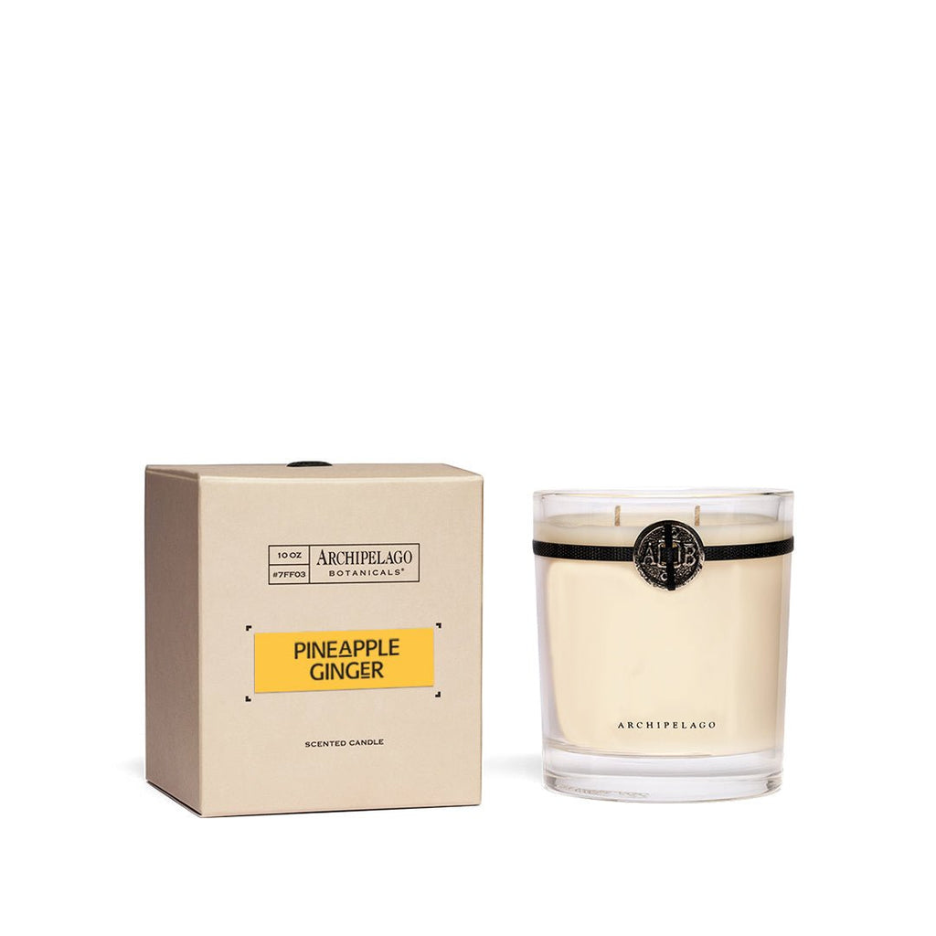 The Archipelago - Pineapple Ginger Credenza 10oz Candle, featuring a tropical scent, is showcased with its minimalist beige box. It comes in a clear glass container adorned with a decorative seal, while the elegant Pineapple Ginger label on both pieces reflects refined simplicity.