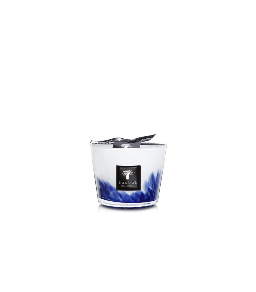 The Baobab - Feathers Touareg Max 10 Candle features a glass holder with a white top, blue feather design at the base, and exudes Sahara fragrance. A black ribbon with a labeled tree logo decorates it, all set against a plain white background to highlight its elegance.