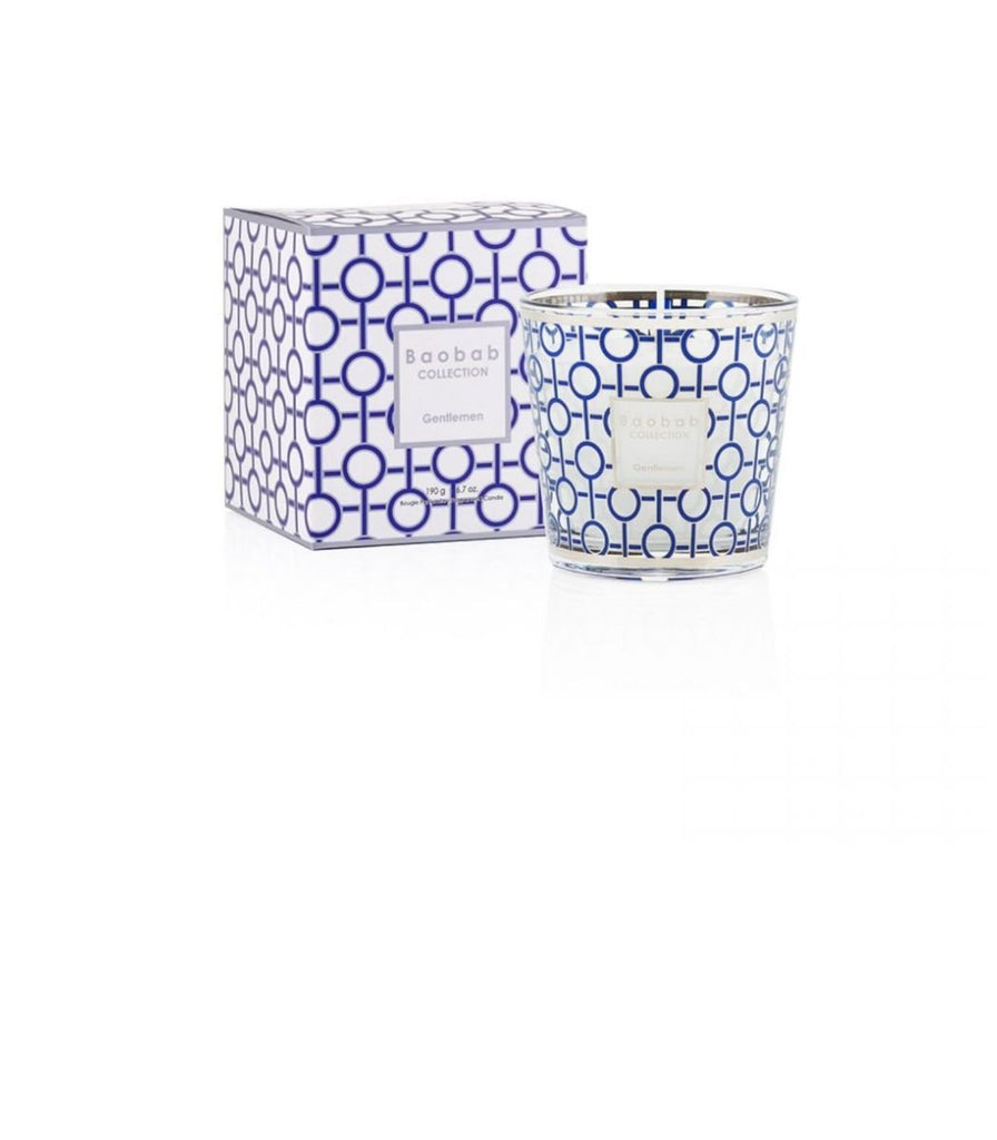 The Boabab - My First Baobab Gentlemen 6.7oz Candle by Baobab features a rum scent in a glass holder with blue and white geometric patterns. The masculine aroma complements its matching box, both displaying the design and brand on a plain white background.