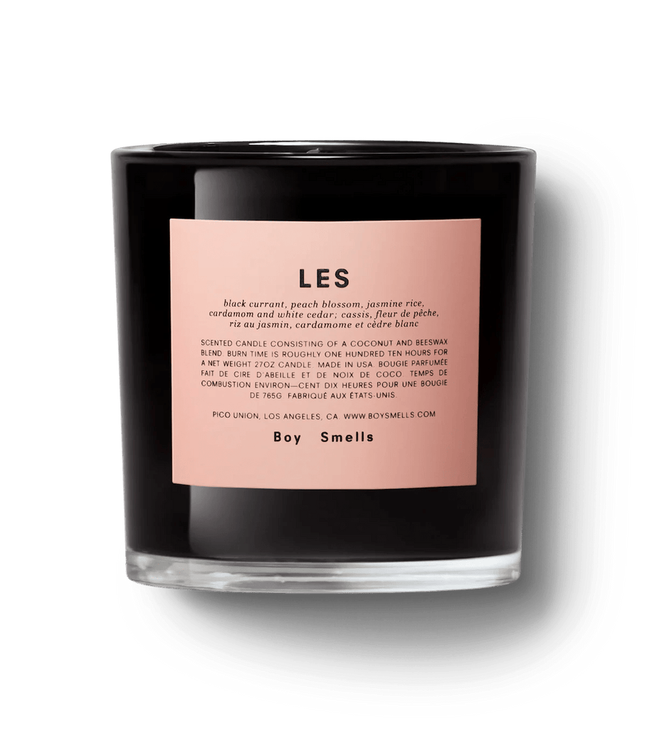 The Boy Smells Ash 27oz Candle features a black container with a pink label displaying Boy Smells. It has woodsy notes of black currant, peach blossom, jasmine rice, and cardamom, wrapped in coconut and beeswax.