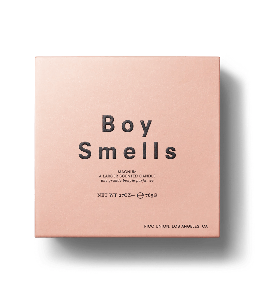 The Boy Smells Ash 27oz Candle comes in a square, light pink box with Boy Smells in bold black text. It features a woodsy fragrance with charred clove notes and is crafted from coconut and beeswax. The bottom right corner notes Pico Union, Los Angeles.