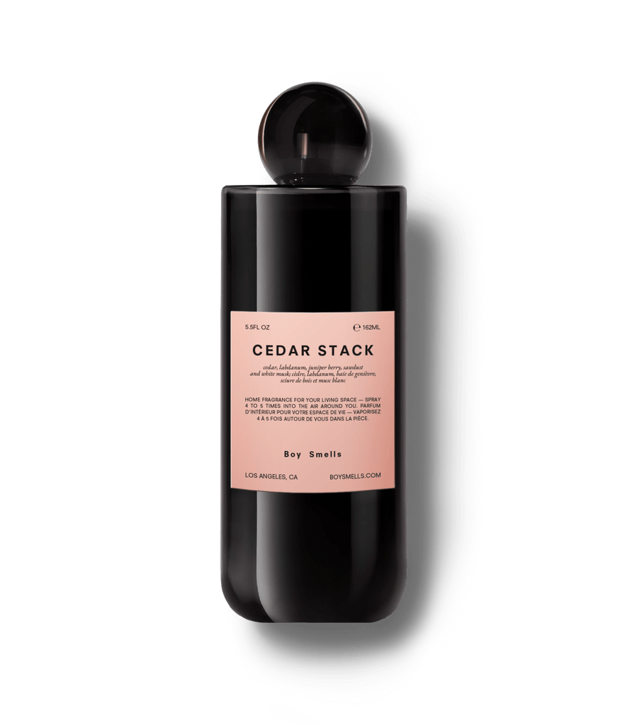 A sleek, black bottle from Boy Smells features a pink Cedar Stack label. This 5.5oz room spray fills your space with a rich cedar wood scent, creating an inviting aroma.