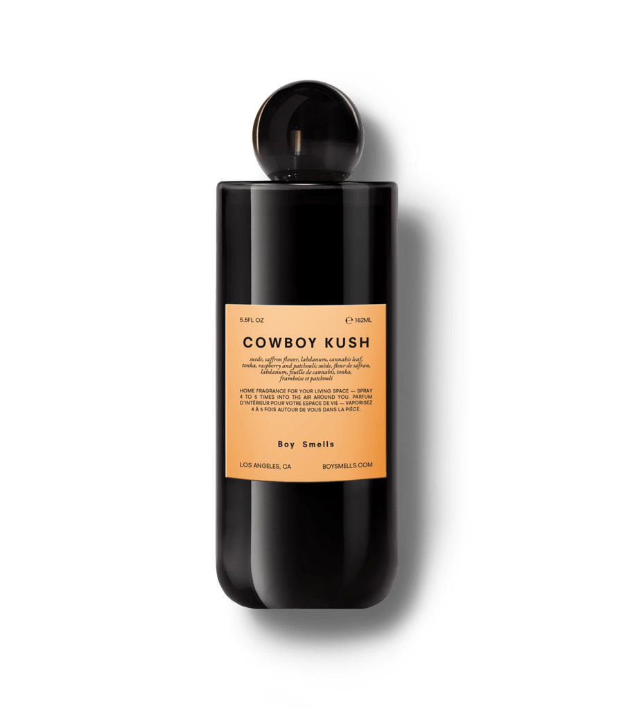 A black cylindrical Cowboy Kush room spray bottle by Boy Smells features a peach label detailing suede and saffron notes, enriched with earthy/spicy essence.