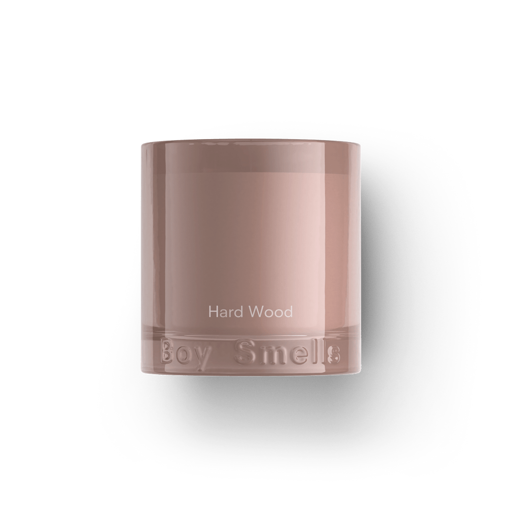 The Boy Smells - Hard Wood 8.5oz Candle features a mauve glass holder with Hard Wood on the front, Boy Smells embossed at the base, and notes of black pepper and cedarwood.