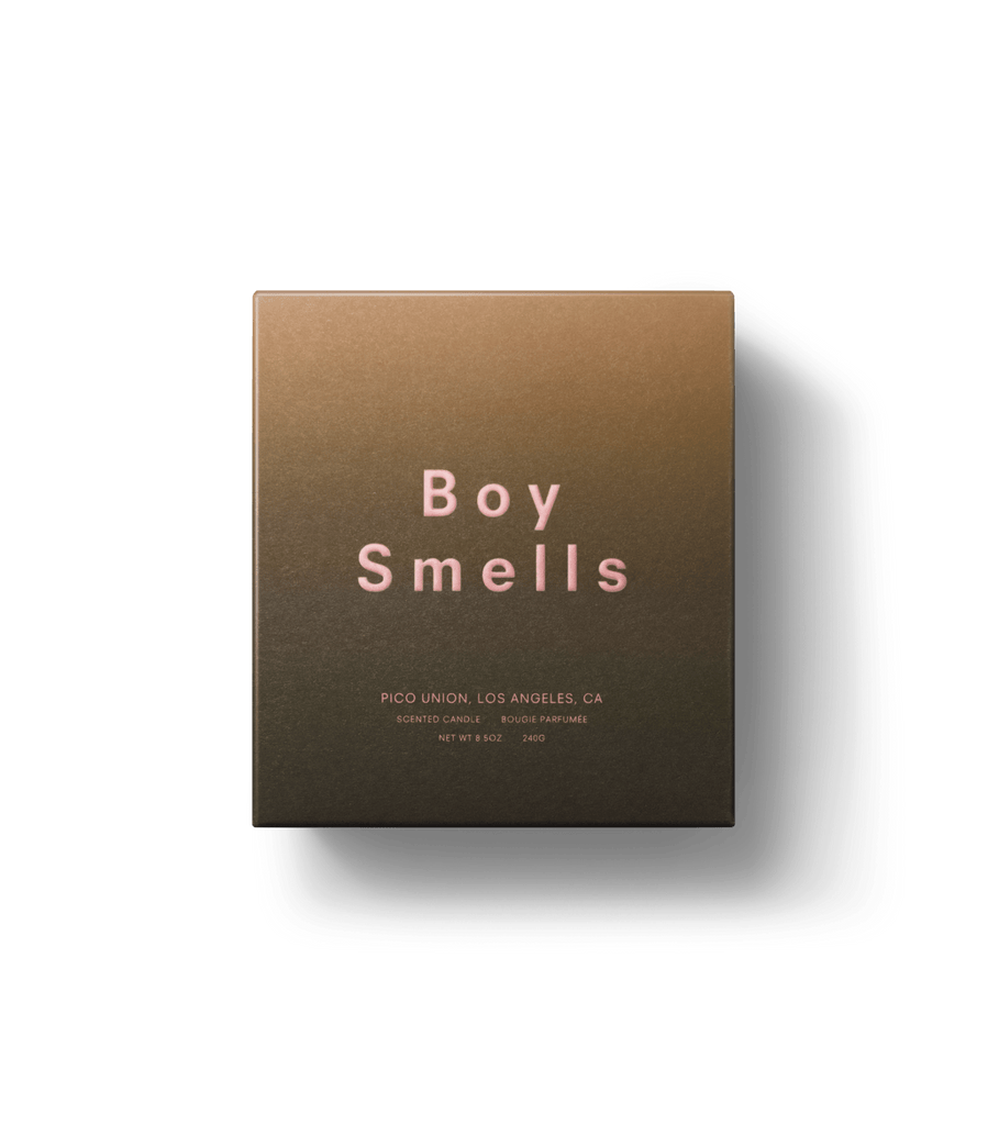 The 8.5oz Boy Smells - Mandarin Fantôme candle comes in a brown box with Boy Smells in pink on it, featuring smoked Mandarin peel scent. Below is smaller text saying Pico Union, Los Angeles, CA and Scented Candle, all set against a gradient background for a minimalist touch.