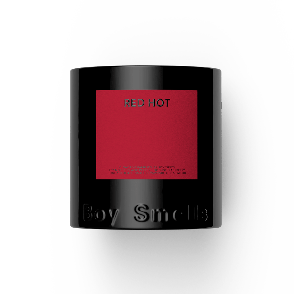 A black Boy Smells candle jar with a red square and "RED HOT" in silver letters sits against a white background; it's the bold, fruity-spicy Red Hot 27oz Candle by Boy Smells.
