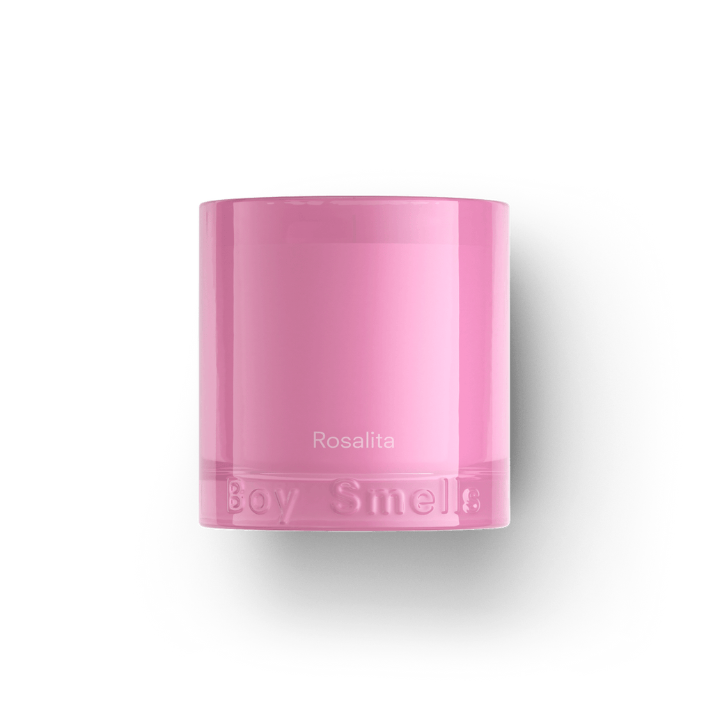 The Boy Smells - Rosalita 8.5oz Candle features a pink hue in a glass holder with Rosalita on the front and Boy Smells embossed at the base. Infused with a rose-domme scent, it is shown against a plain white background.