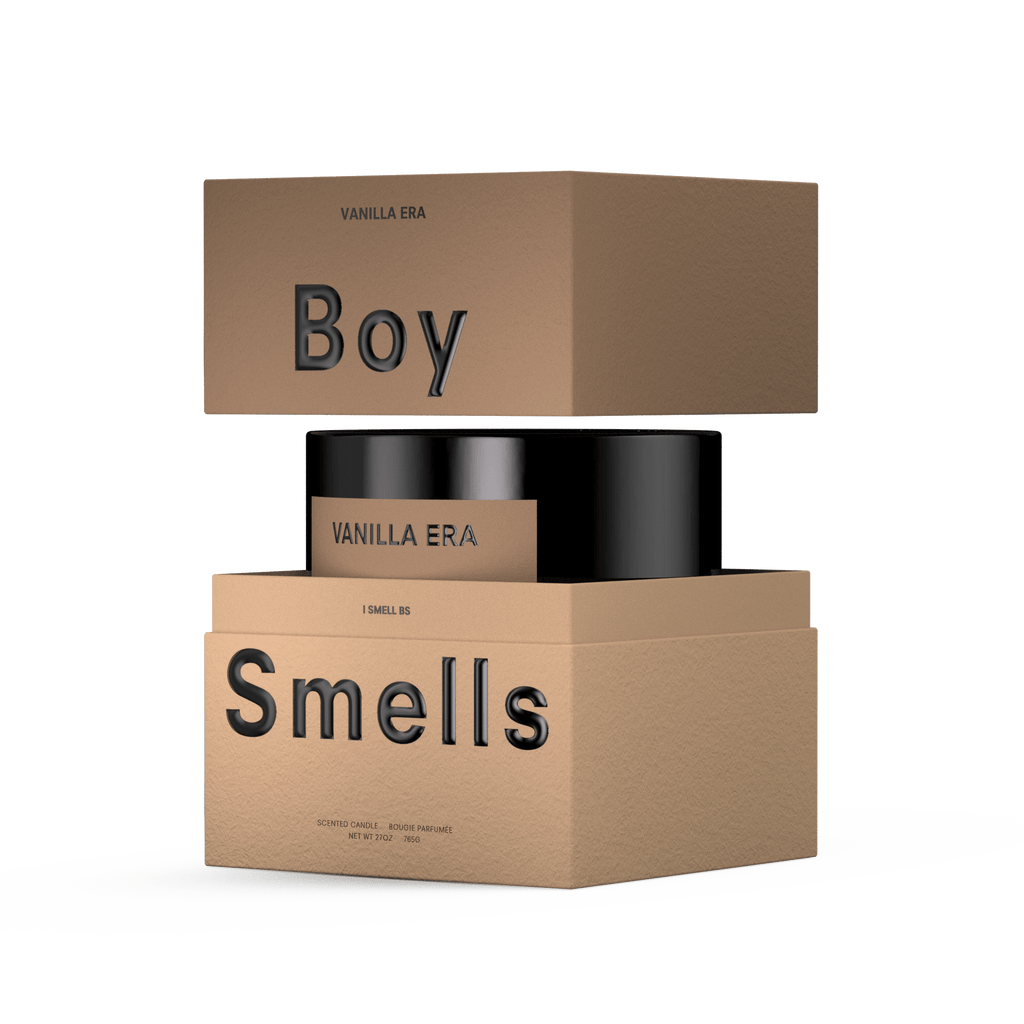 A brown Boy Smells – Vanilla Era 27oz Candle box sits above a black vanilla candle jar, with another brown box below labeled "Smells." Packaging features minimalist black VANILLA ERA text on white, evoking a gourmand scent and long burn time.