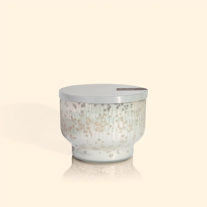 The Capri BLUE - Chestnut Embers Holiday Mercury Inverted Jar 10 oz Candle, set against a light beige background, showcases a speckled beige and off-white textured pattern reminiscent of chestnut embers. Its smooth lid complements the jars soothing color palette flawlessly.