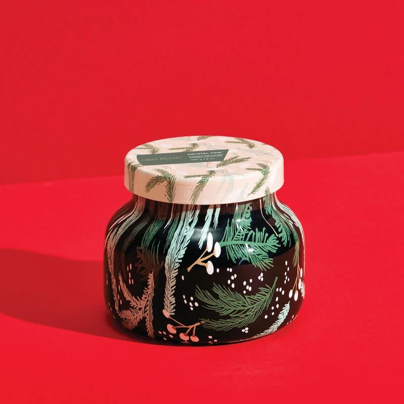 The Capri BLUE - Crystal Pine Holiday Pattern Play Petite Jar 8 oz Candle features a festive design with green pine branches and white berries on a dark background, accompanied by a lid with the same holiday pattern set against a vibrant red backdrop.